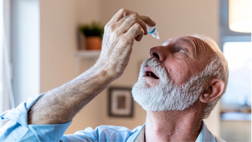 an older man administers eye drops as part of his cataract surgery recovery
